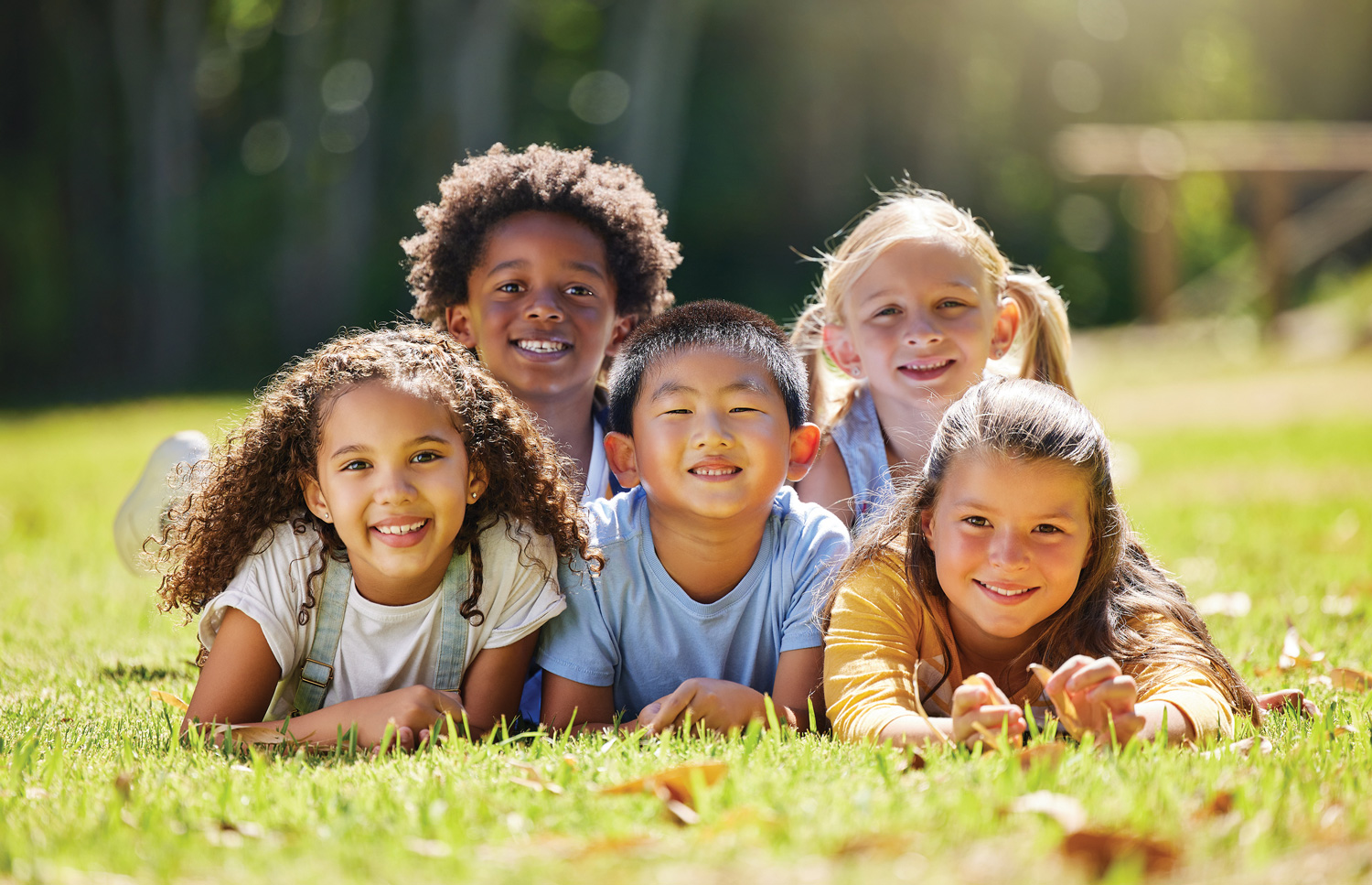 Group of elementary aged children lay piled together on grass.